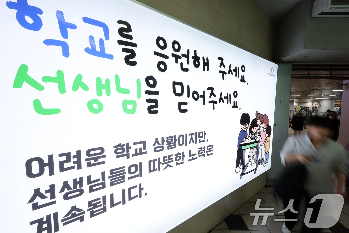 본문 이미지 - 서이초 교사 순직 1주기(18일)를 앞둔 16일 서울 중구 봉래동 지하철 서울역에 실천교육교사모임이 모금을 통해 게시한 추모 광고 앞으로 시민이 지나고 있다. 2024.7.16/뉴스1 ⓒ News1 박정호 기자