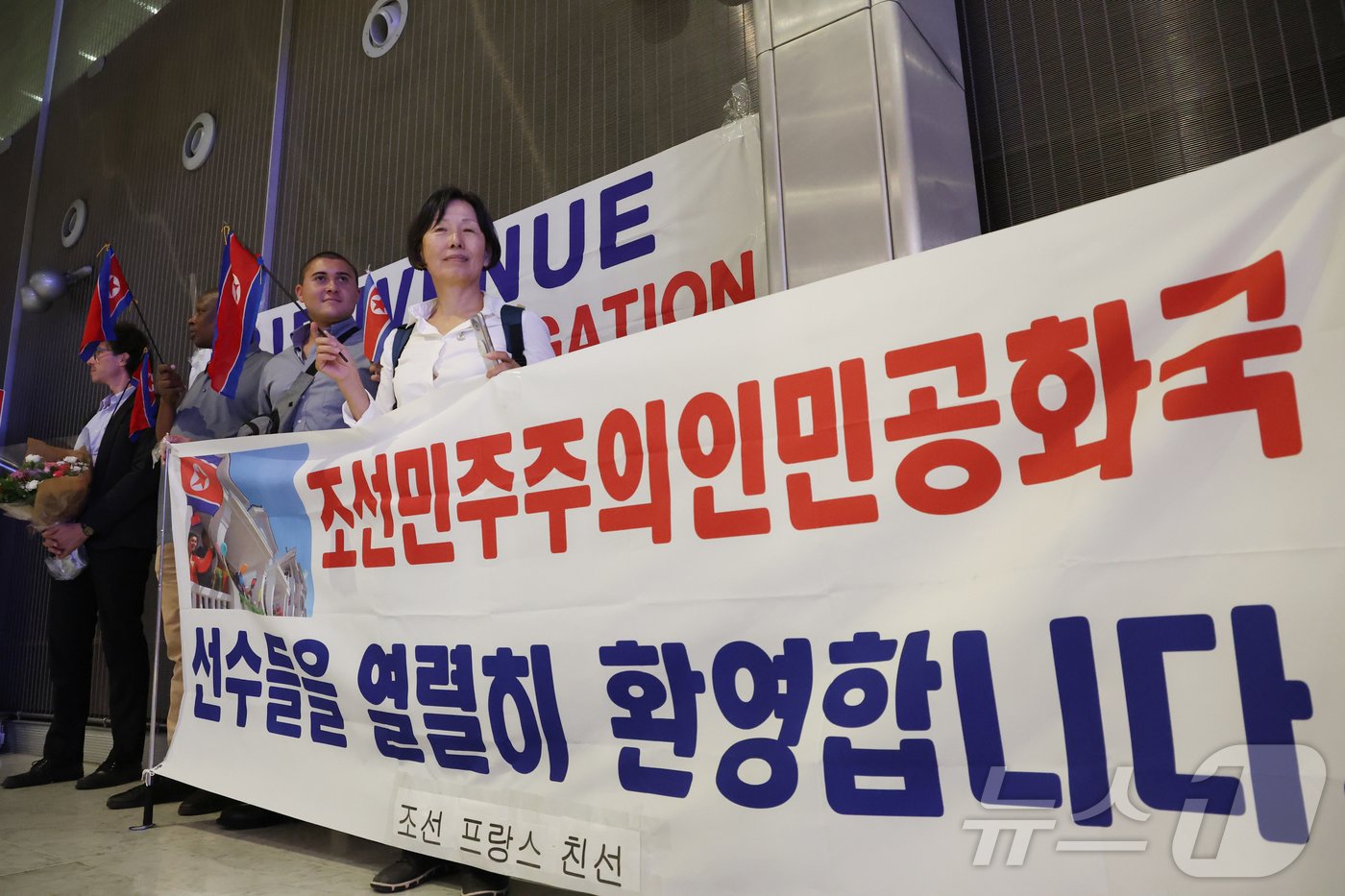 본문 이미지 - 프랑스·조선 친선 관계자들이 21일 오후(한국시간) 프랑스 파리 샤를 드골 공항을 통해 입국하는 2024 파리올림픽 북한 선수단을 환영하고 있다. 2024.7.21./뉴스1 ⓒ News1 박정호 기자