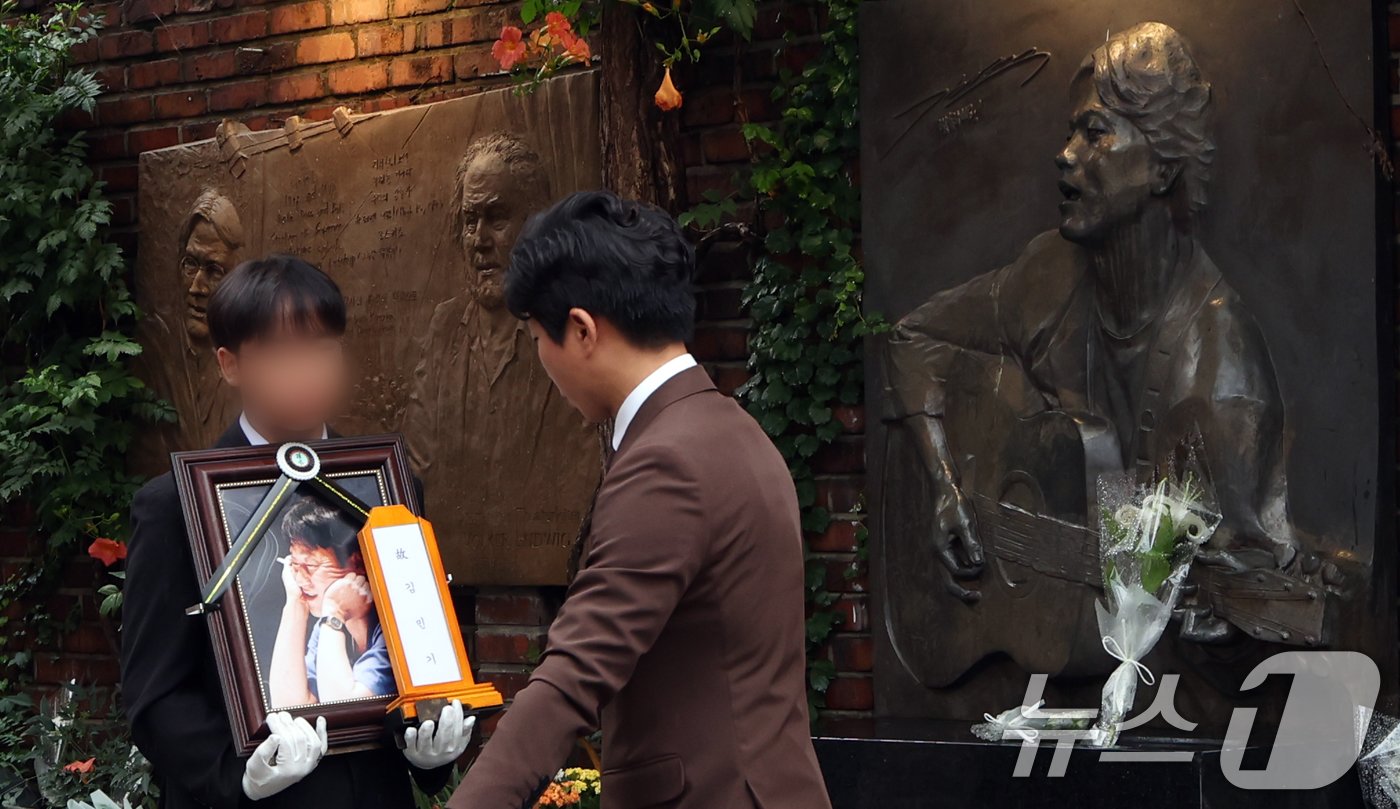 본문 이미지 - 20일 서울 종로구 대학로 아르코 꿈밭극장(옛 학전)에서 열린 고 김민기의 노제에서 고인의 영정이 김광석 부조상 앞으로 지나가고 있다. 2024.7.24/뉴스1 ⓒ News1 김명섭 기자