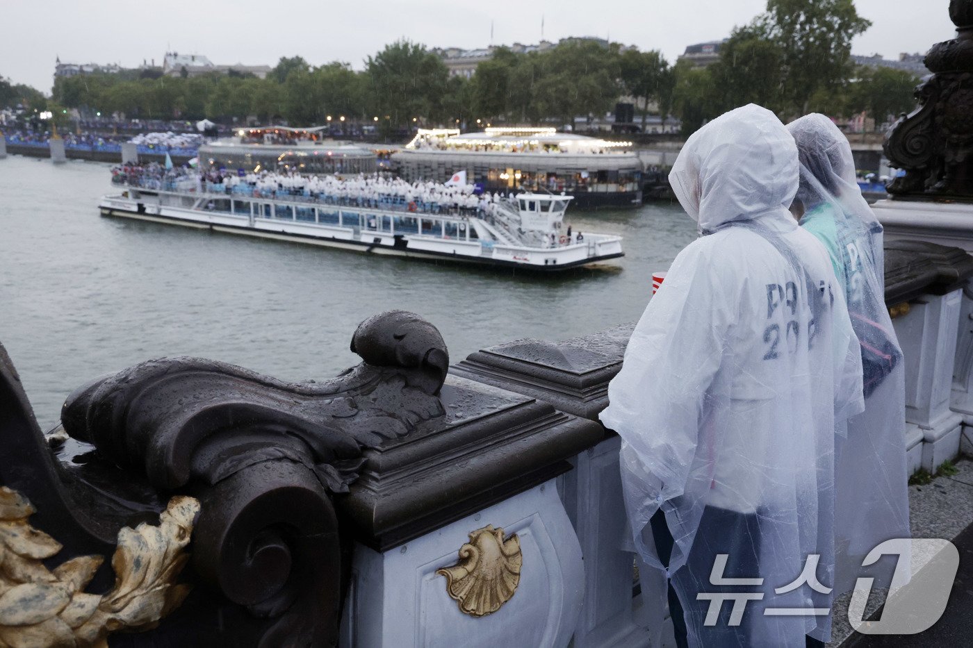 본문 이미지 - 2024 파리 올림픽 개회식이 열린 27일(한국시각) 프랑스 파리 센강에서 자원봉사자들이 우비를 입고 각국 선수단의 수상 행진을 지켜보고 있다. (공동취재) 2024.7.27/뉴스1 ⓒ News1 이동해 기자