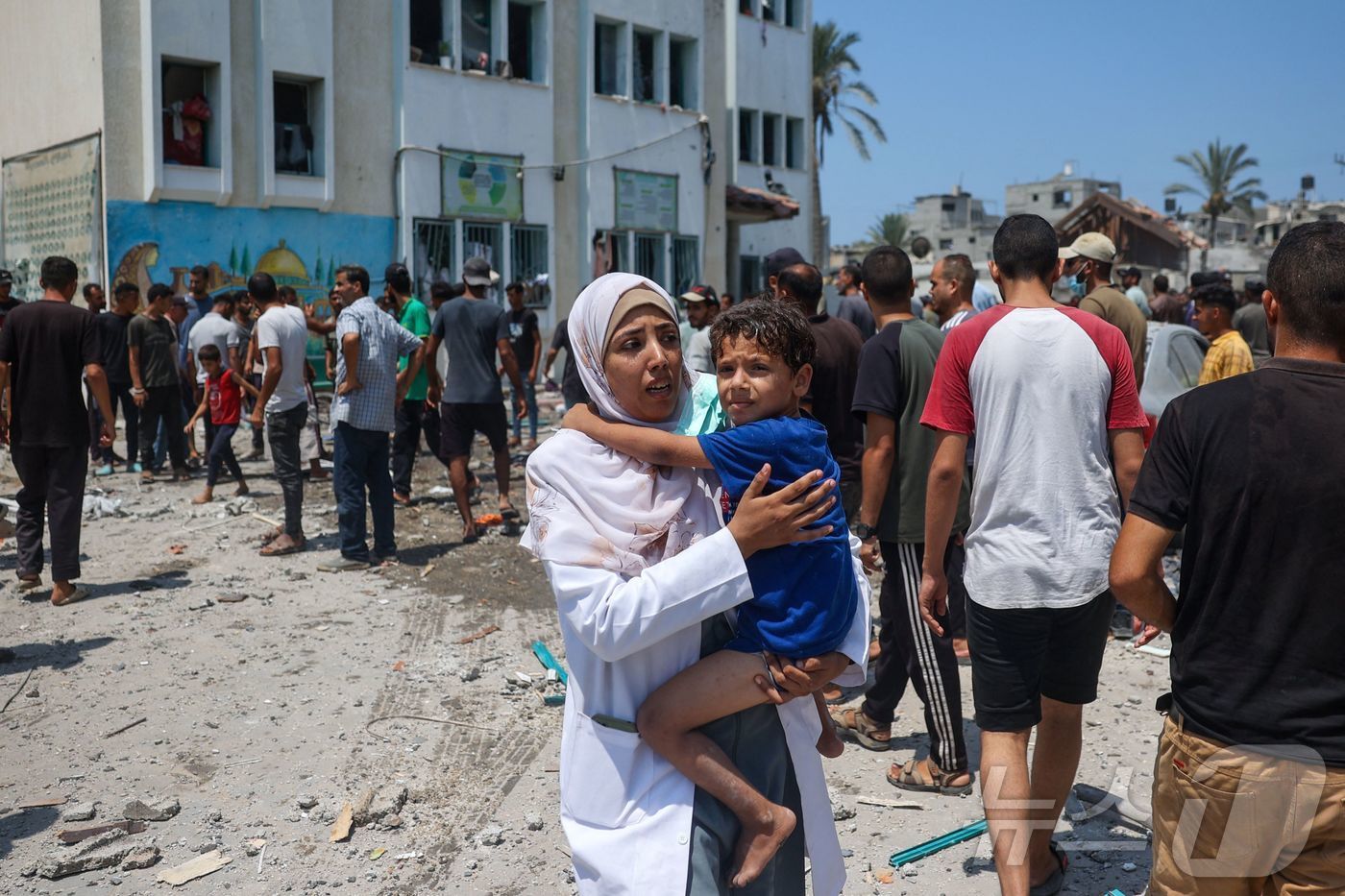 본문 이미지 - 27일(현지시간) 가자지구 중부 데이르알발라에서 한 여성이 아이를 안고 대피하고 있다. 이날 이스라엘군은 이곳 카디자 학교에 팔레스타인 무장 정파 하마스 대원이 은신하고 있다는 이유를 들어 공습을 퍼부었고, 이로 인해 최소 30명이 숨지고 100명상이 다쳤다. 2024.07.27/ ⓒ AFP=뉴스1 ⓒ News1 권진영 기자