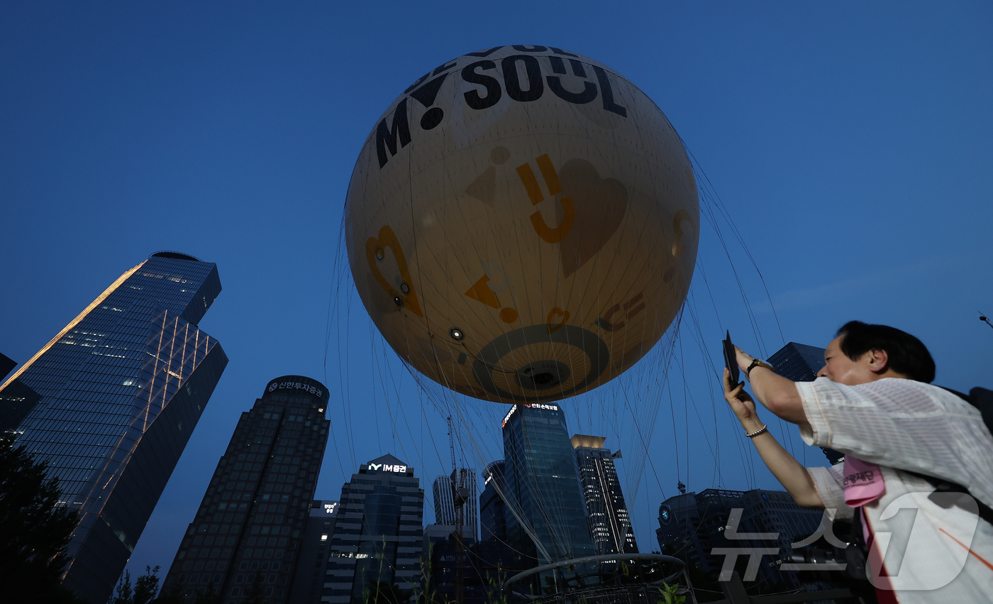 (서울=뉴스1) 김도우 기자 = 10일 서울 영등포구 여의동공원에서 열린 계류식 가스기구 '서울달' 개장식에서 시민들이 서울달을 관람하고 있다.이날 개장한 '서울달'은 최고 130 …