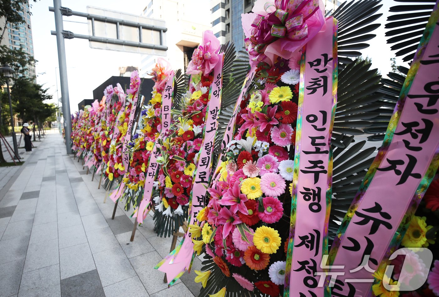 본문 이미지 - 18일 오전 서울 용산구 하이브 사옥 앞에 전동스쿠터 음주운전 혐의로 입건된 방탄소년단(BTS) 멤버 슈가(31·민윤기)의 탈퇴를 촉구하는 일부 팬들의 화환이 놓여 있다. 2024.8.18/뉴스1 ⓒ News1 오대일 기자