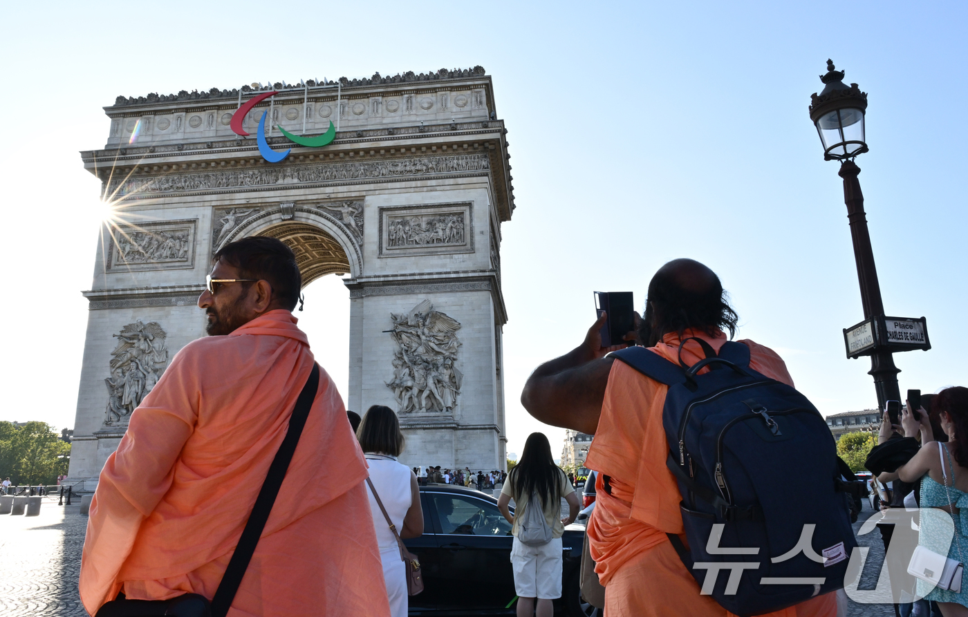 (서울=뉴스1) 사진공동취재단 = 2024 파리하계패럴림픽을 하루 앞둔 27일(현지시간) 관광객들이 패럴림픽 엠블럼 ‘아지토스’가 걸린 프랑스 파리 에투알 개선문을 배경으로 기념사 …