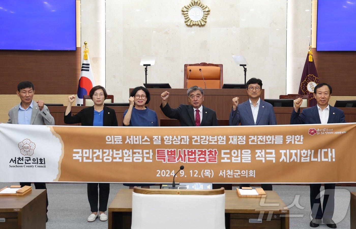 본문 이미지 - 서천군의원들이 12일 본회의장에서 국민건강보험공단 특별사법경찰제도 도입을 지지하는 내용의 현수막을 들고 있다. (서천군의회 제공) /뉴스1