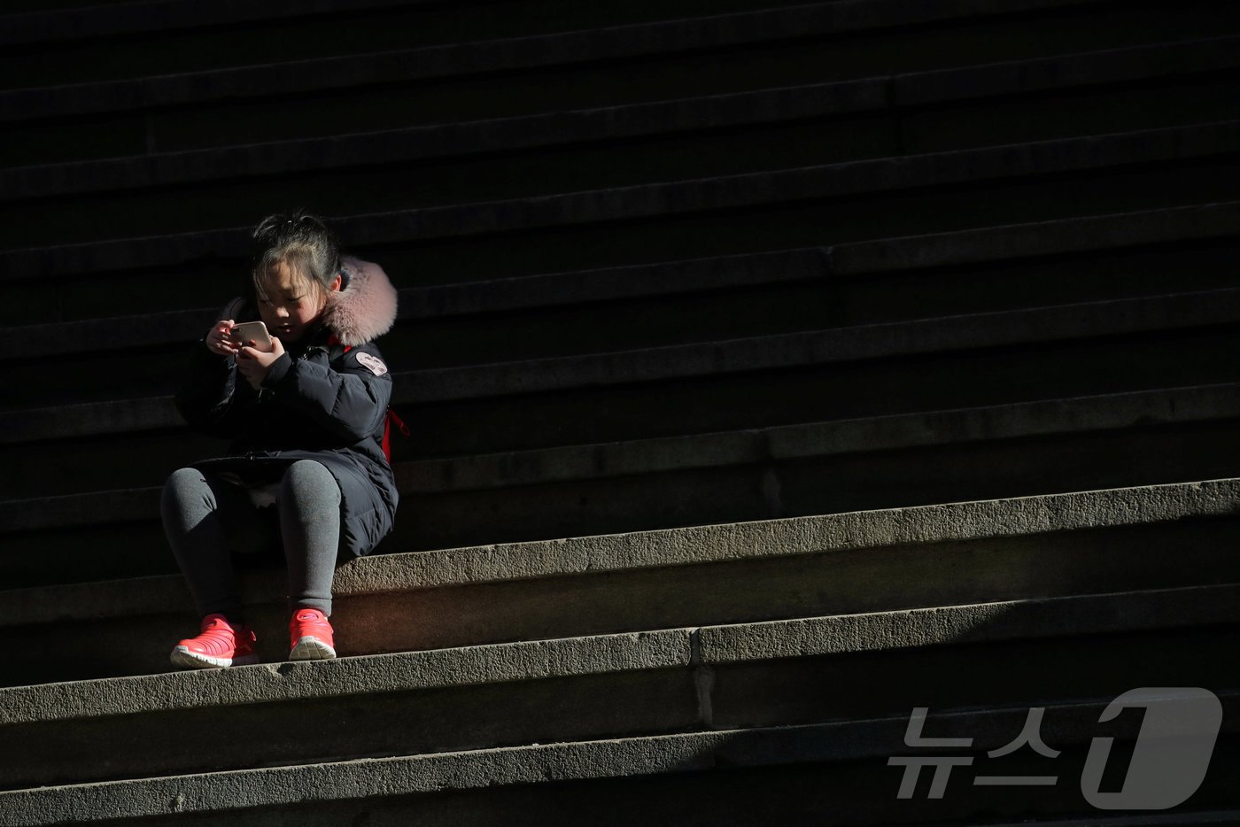 본문 이미지 - 미국 뉴욕 월스트리트에서 한 어린이가 계단에 걸터앉아 스마트폰을 사용하고 있다. 2019.02.19/ ⓒ 로이터=뉴스1 ⓒ News1 권진영 기자