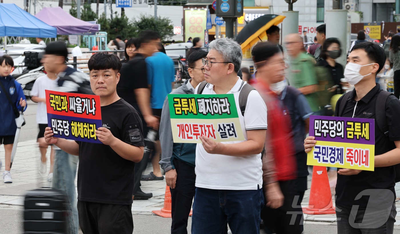 (서울=뉴스1) = 한국주식투자자연합회 회원들이 21일 오후 서울 중구 서울역 광장에서 금융투자소득세 도입을 반대하는 피켓을 들어보이고 있다. 2024.9.21/뉴스1