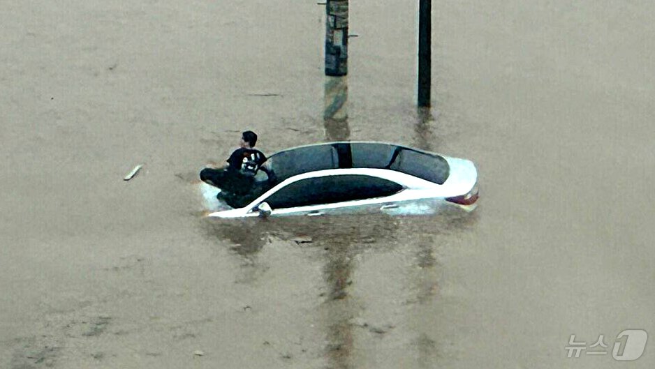 본문 이미지 - 지난 21일 호우특보가 발효된 경남 김해에서 도로가 침수돼 한 남성이 차량 위로 대피해있다. 아래엔 흙탕물이 높게 차올라 차량 보닛이 거의 다 잠긴 상태다. 글 작성자는 김해 내덕동에서 사진을 촬영했다고 밝히며 "도로 앞은 지하차도, 옆은 산이라 물이 갑자기 불어나 피해를 입은 것 같다＂고 설명했다.(온라인 커뮤니티)2024.9.22/뉴스1
