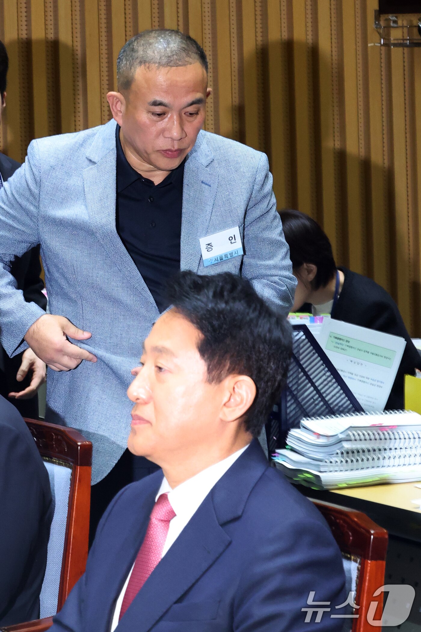 본문 이미지 - &#39;정치 브로커&#39; 명태균씨가 23일 오후 서울 중구 서울시청에서 열린 국회 행정안전위원회 서울시청 국정감사에서 의원질의를 마치고 오세훈 서울시장 뒤로 이동하고 있다. 2025.10.23/뉴스1 ⓒ News1 황기선 기자
