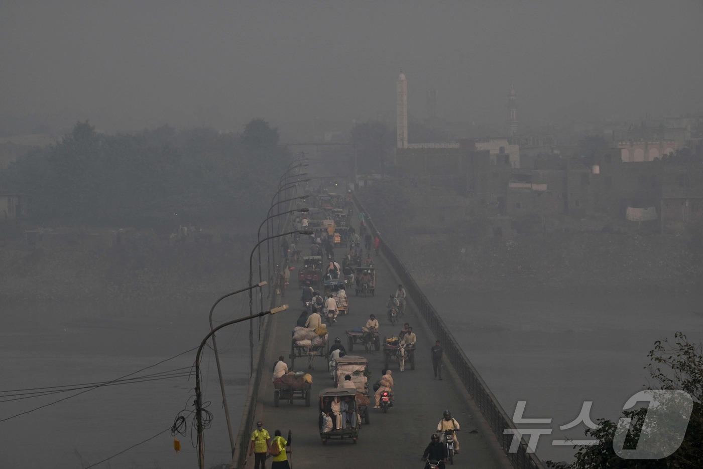 (라호르 AFP=뉴스1) 이정환 기자 = 27일(현지시간) 파키스탄 라호르에서 짙은 스모그 속 통근자들이 다리를 건너고 있다. 2025.10.,27.ⓒ AFP=뉴스1