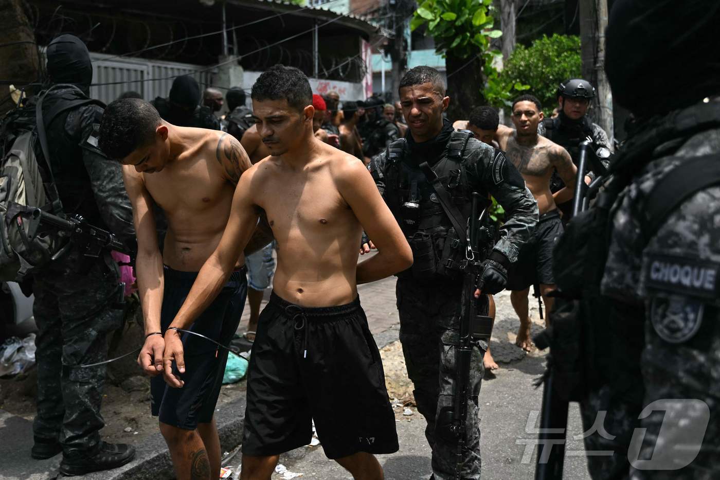 본문 이미지 - 28일&#40;현지시간&#41; 브라질 리우데자네이루 페냐에서 진행된 봉쇄 작전 중 체포된 범죄자들을 경찰관들이 호송하고 있다. 2025.10.28. ⓒ AFP=뉴스1 ⓒ News1 이정환 기자