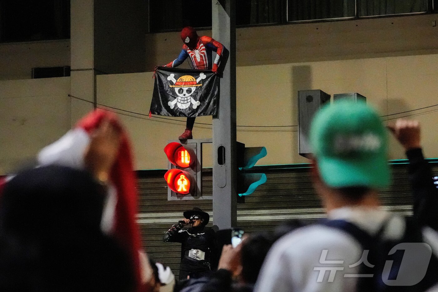 본문 이미지 - 9월 28일&#40;현지시간&#41; 페루 리마에서 스파이더맨 복장을 한 시위 참가자가 만화 &#39;원피스&#39;의 &#39;밀짚모자 해적단&#39; 깃발을 들고 신호등 위에 올라서 있다. 2025.09.28. ⓒ 로이터=뉴스1 ⓒ News1 윤다정 기자