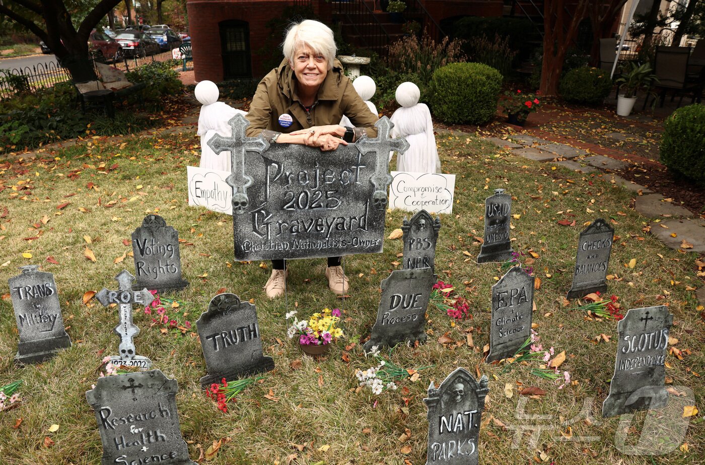 본문 이미지 - 29일&#40;현지시간&#41; 미국 워싱턴DC 주민 도나 브레슬린&#40;79&#41;이 도널드 트럼프 미국 대통령을 풍자·비판하는 내용의 묘비로 꾸민 앞마당에 서 있다. 2025.10.29. ⓒ 로이터=뉴스1 ⓒ News1 윤다정 기자