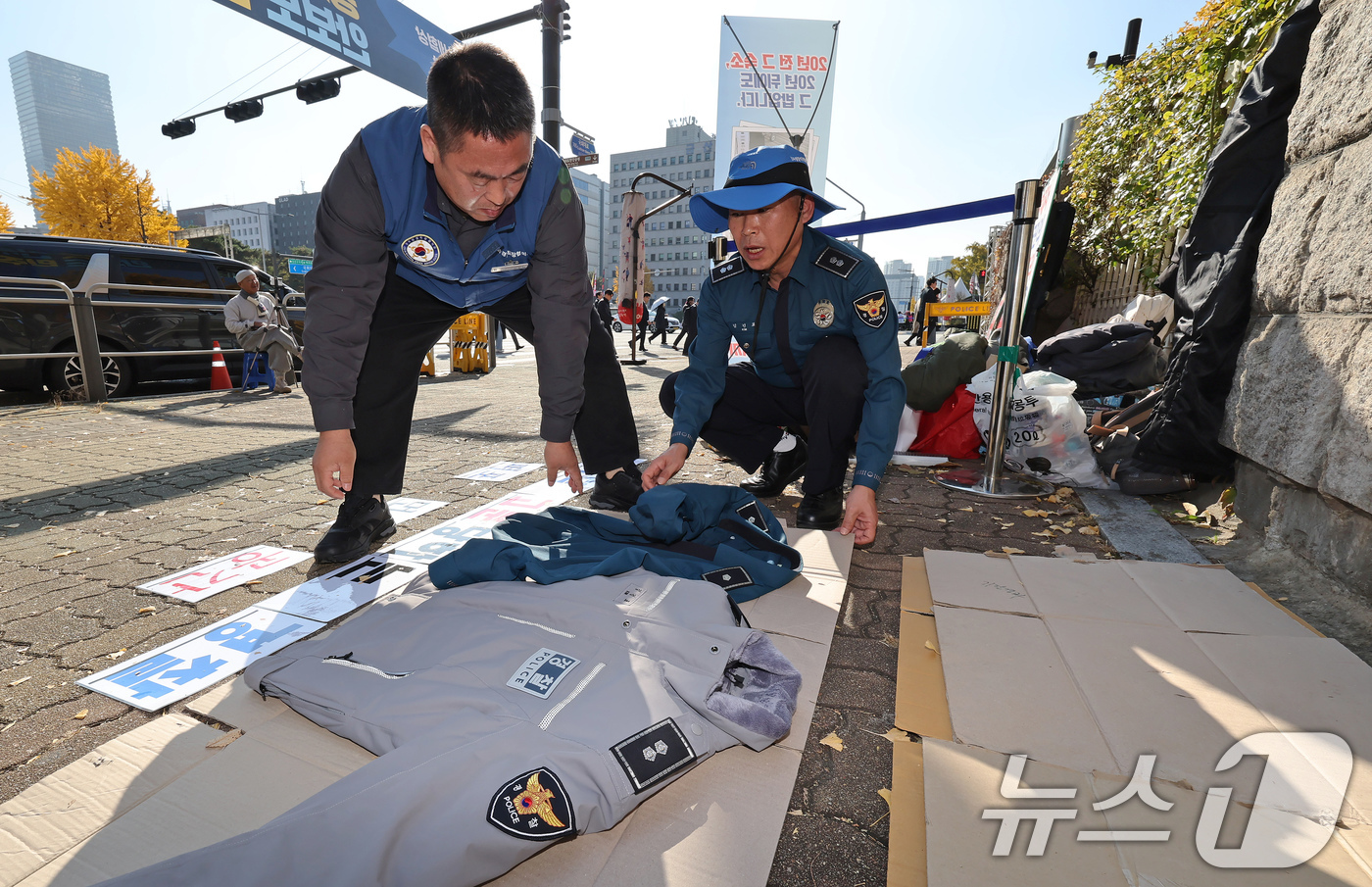 (서울=뉴스1) 장수영 기자 = 12일 오후 서울 여의도 국회 정문에서 열린 경주 APEC 2025 경찰 숙소·식사 실태 비판 사진전에서 관계자가 바닥에 깔아 놓은 종이 상자 위에 …