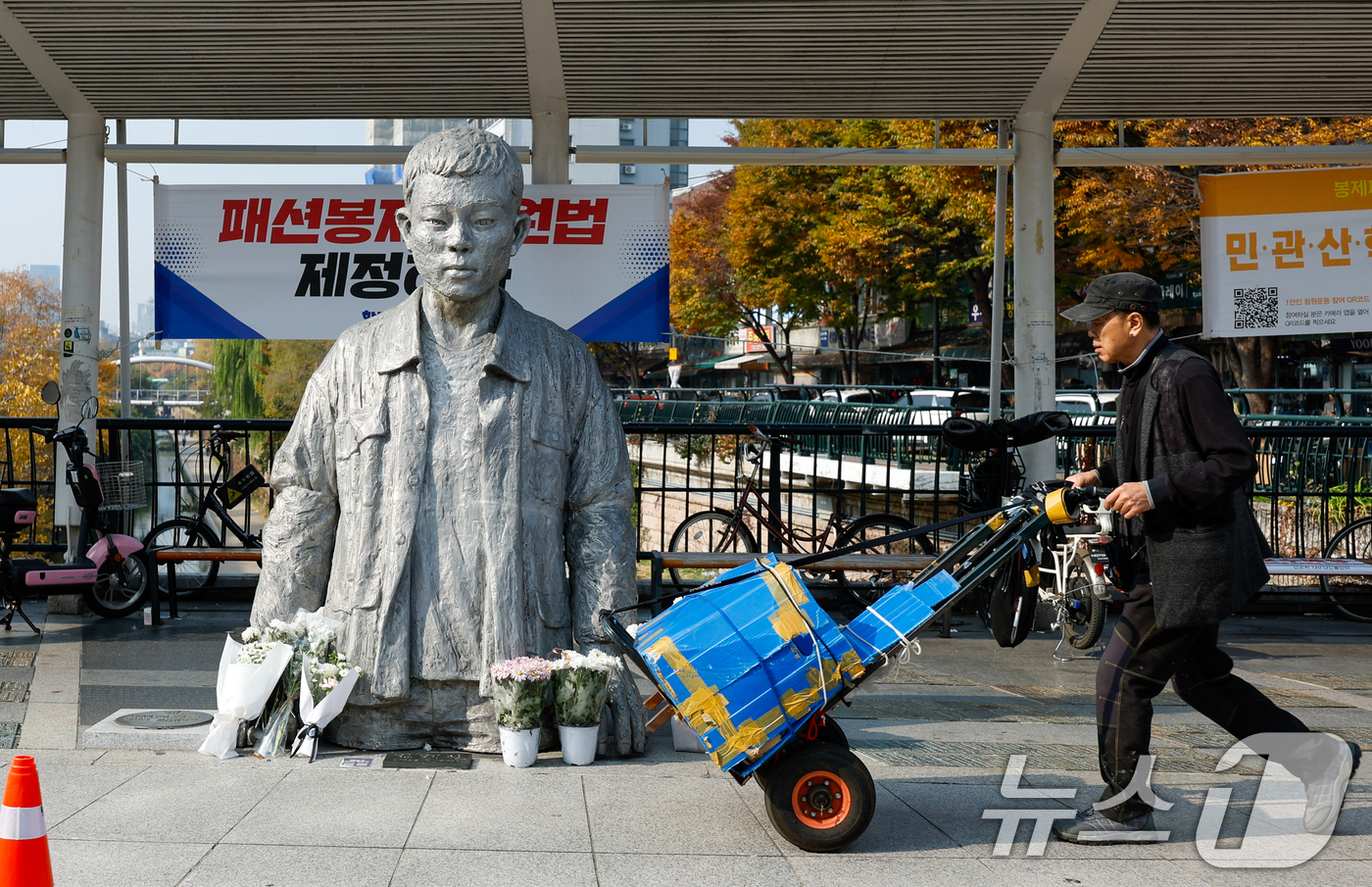 (서울=뉴스1) 안은나 기자 = 전태일 열사 55주기인 13일 서울 종로구 전태일다리 전 열사 동상 뒤로 패션봉제 지원법 제정을 촉구하는 현수막이 걸려 있다. 2025.11.13/ …