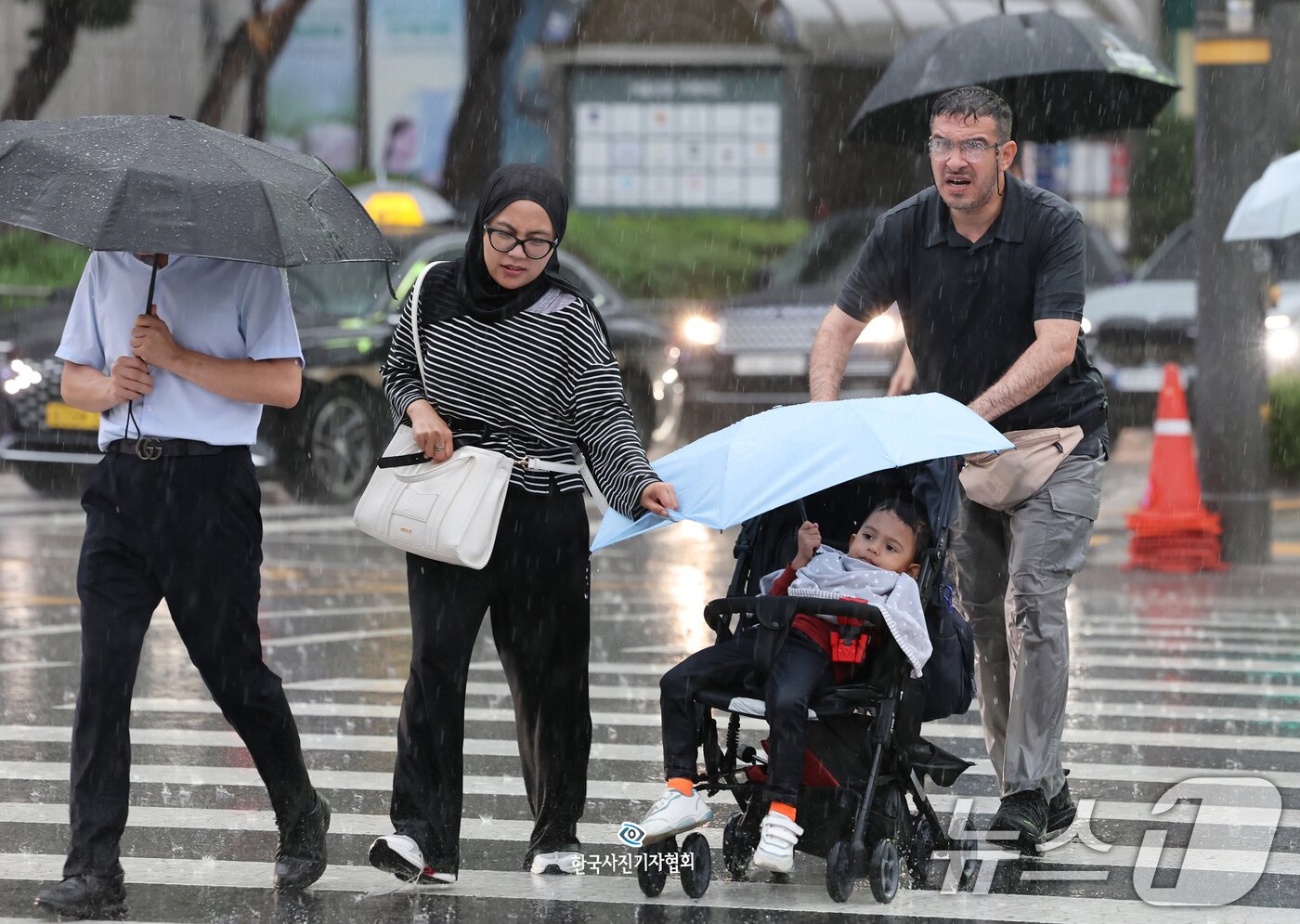 본문 이미지 - 요란한 가을비가 내린 9월 16일 오후 서울 중구 서울시청 앞을 지나는 외국인 부모가 유모차를 탄 아이에게 우산을 씌워준 채 급히 발걸음을 옮기고 있다.