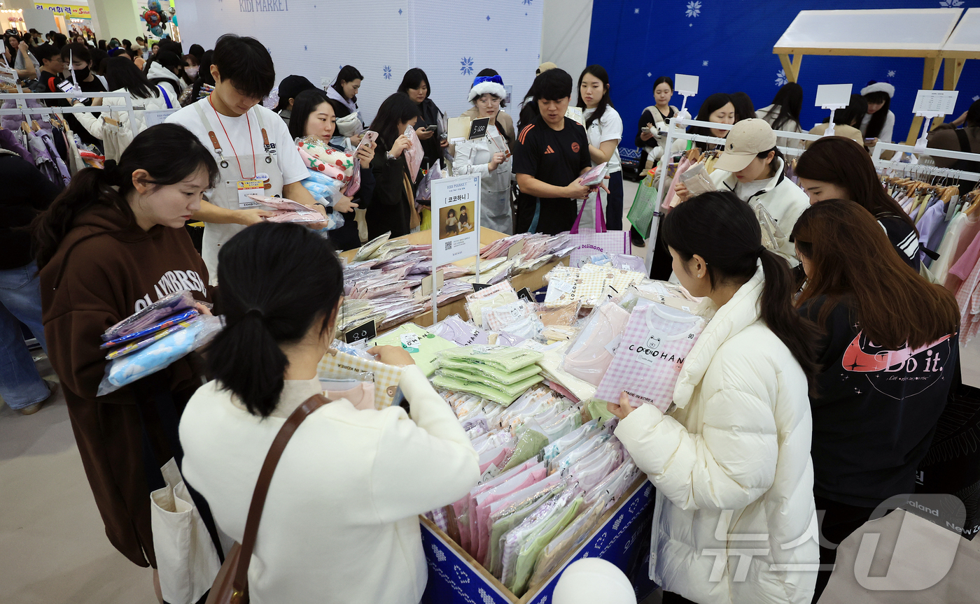 (서울=뉴스1) 김진환 기자 = 13일 오후 서울 강남구 코엑스에서 열린 제56회 서울국제유아교육전 및 키즈페어를 찾은 관람객이 아이 옷을 고르고 있다. 2025.11.13/뉴스1 …