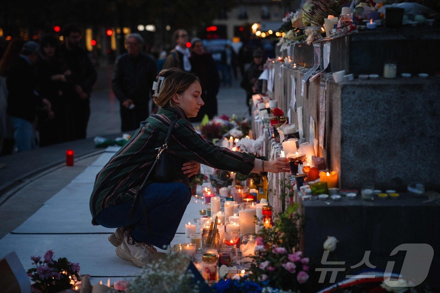본문 이미지 - 11일&#40;현지시간&#41; 파리 레퓌블리크 광장에 마련된 임시 추모비에서 한 여성이 테러 희생자들을 추모하며 꽃을 헌화하고 촛불을 밝히고 있다. 2025.11.11 ⓒ AFP=뉴스1 ⓒ News1 이정환 기자