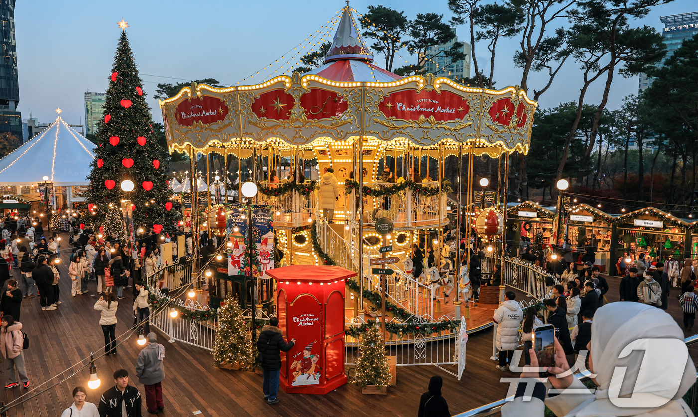 (서울=뉴스1) 이호윤 기자 = 20일 서울 송파구 롯데월드타워 월드파크 잔디광장에서 열린 '롯데타운 크리스마스 마켓'을 찾은 시민들이 크리스마스트리와 회전목마등 다양한 볼거리를 …
