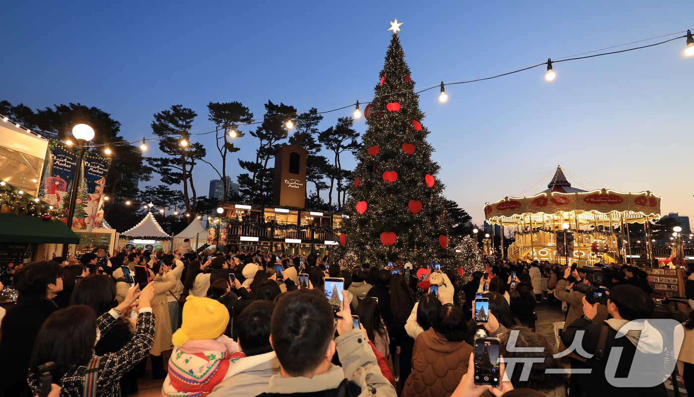 (서울=뉴스1) 이호윤 기자 = 20일 서울 송파구 롯데월드타워 월드파크 잔디광장에서 열린 '롯데타운 크리스마스 마켓'을 찾은 시민들과 관광객들이 크리스마스 트리를 촬영하고 있다. …