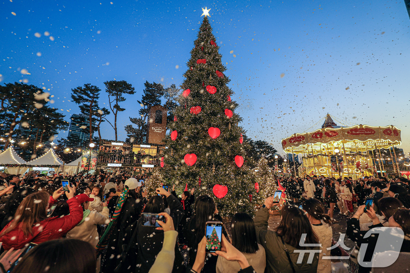 (서울=뉴스1) 이호윤 기자 = 20일 서울 송파구 롯데월드타워 월드파크 잔디광장에서 열린 '롯데타운 크리스마스 마켓'을 찾은 시민들과 관광객들이 인공눈을 맞으며 사진촬영을 하고 …