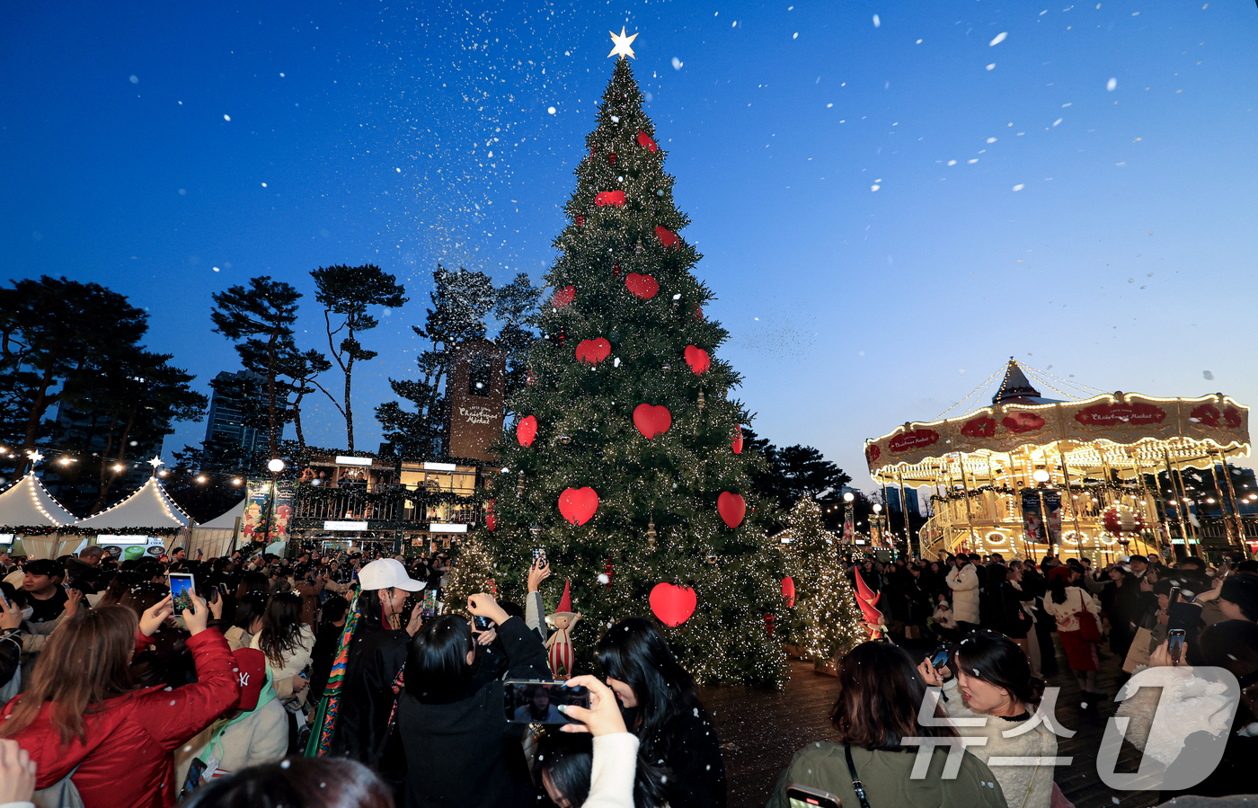 (서울=뉴스1) 이호윤 기자 = 20일 서울 송파구 롯데월드타워 월드파크 잔디광장에서 열린 '롯데타운 크리스마스 마켓'을 찾은 시민들과 관광객들이 인공눈을 맞으며 사진촬영을 하고 …