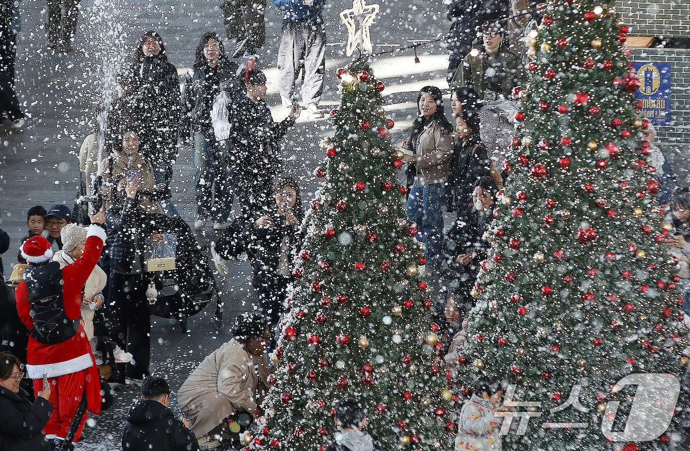(부산=뉴스1) 윤일지 기자 = 27일 부산 해운대구 영화의전당에서 열린 '크리스마스 빌리지 부산 2025'를 찾은 시민들이 인공눈을 맞으며 크리스마스 트리를 배경으로 사진을 찍는 …