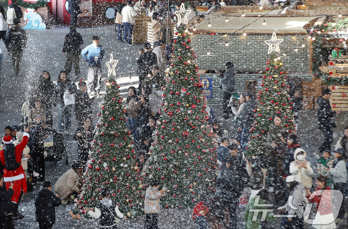 (부산=뉴스1) 윤일지 기자 = 27일 부산 해운대구 영화의전당에서 열린 '크리스마스 빌리지 부산 2025'를 찾은 시민들이 인공눈을 맞으며 크리스마스 트리를 배경으로 사진을 찍는 …