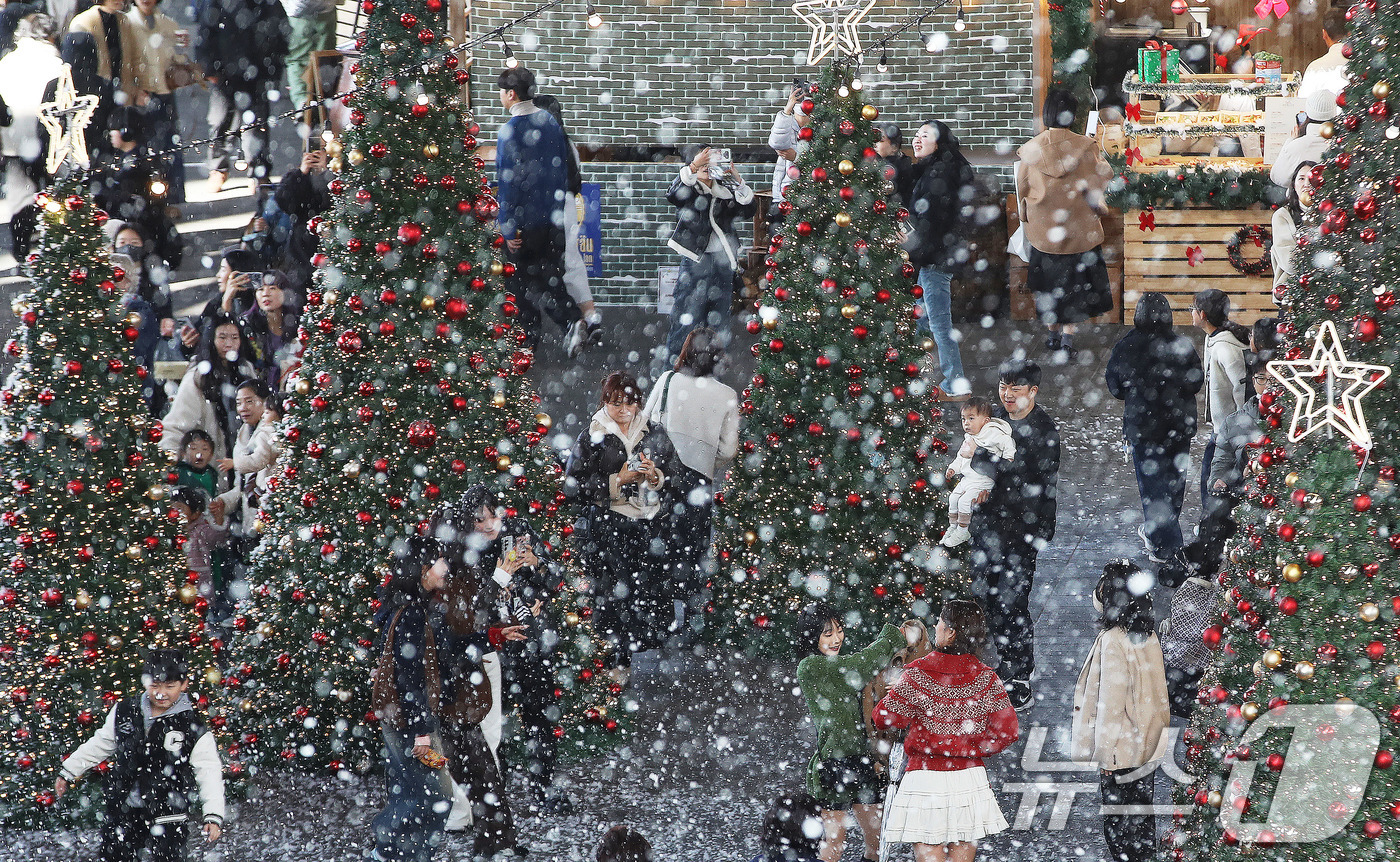 (부산=뉴스1) 윤일지 기자 = 27일 부산 해운대구 영화의전당에서 열린 '크리스마스 빌리지 부산 2025'를 찾은 시민들이 인공눈을 맞으며 크리스마스 트리를 배경으로 사진을 찍는 …
