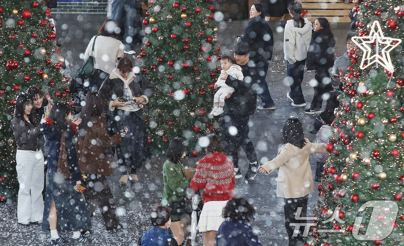 (부산=뉴스1) 윤일지 기자 = 27일 부산 해운대구 영화의전당에서 열린 '크리스마스 빌리지 부산 2025'를 찾은 시민들이 인공눈을 맞으며 크리스마스 트리를 배경으로 사진을 찍는 …