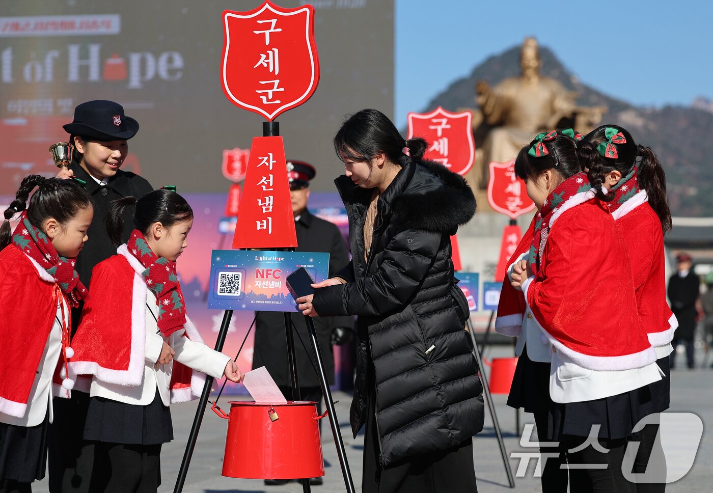 본문 이미지 - 2025 구세군 연말 모금 캠페인이 시작된 28일 오전 서울 광화문광장에서 열린 2025 구세군 자선냄비 시종식에서 서울주니어합창단 어린이들과 학부모가 NFC 모금 시연을 하고 있다.  2025.11.28/뉴스1 ⓒ News1 오대일 기자