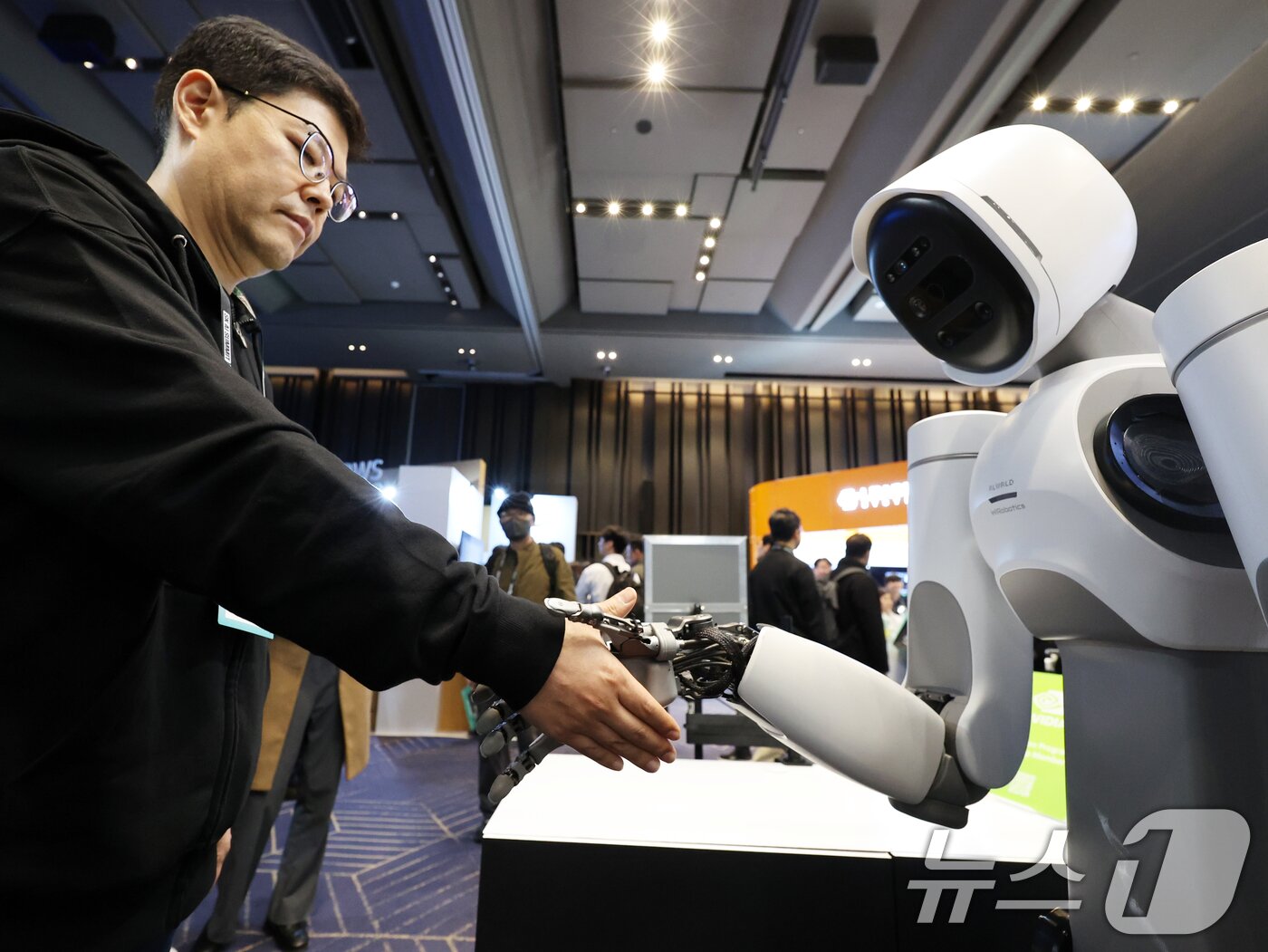 본문 이미지 - 3일 서울 강남구 코엑스에서 열린 ‘SK AI서밋 2025’에서 부스 관계자가 로봇과 악수를 시연하고 있다. 2025.11.3/뉴스1 ⓒ News1 황기선 기자
