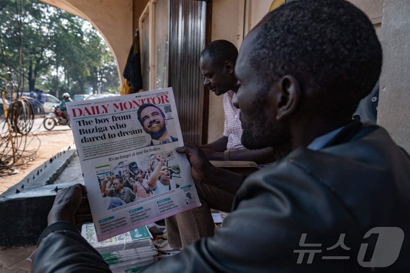 본문 이미지 - 우간다 수도 캄팔라 주민들이 6일 조란 맘다니 민주당 뉴욕시장 후보의 당선 소식을 신문에서 읽고 있다. 사진 속 주민이 읽고 있는 &#39;데일리모니터&#39;는 맘다니가 10대 시절 인턴으로 일했던 신문사다. 2025.11.6 ⓒ AFP=뉴스1 ⓒ News1 강민경 기자
