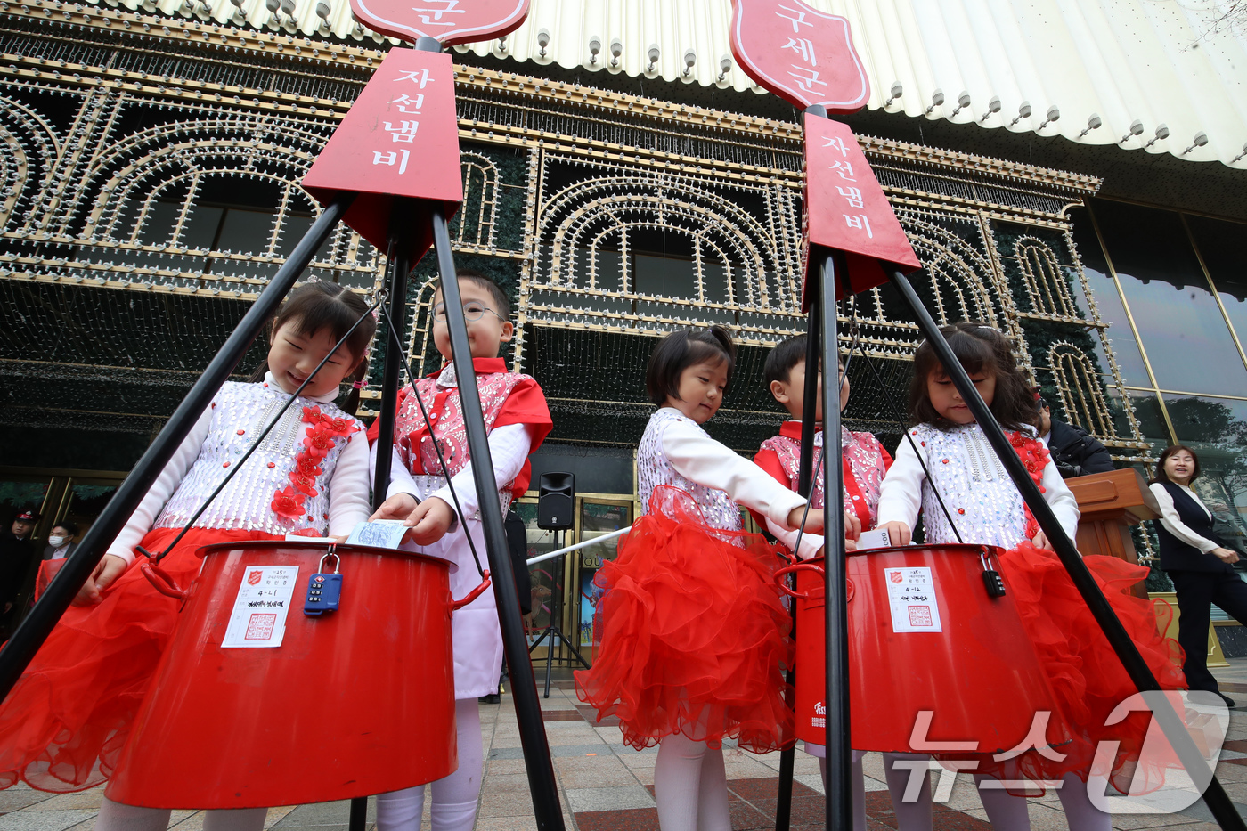 (부산=뉴스1) 윤일지 기자 = 1일 부산 부산진구 롯데백화점 부산본점 정문 앞 광장에서 열린 구세군 자선냄비 시종식에서 축하공연을 펼친 어린이들이 자선냄비에 돈을 넣고 있다.구세 …