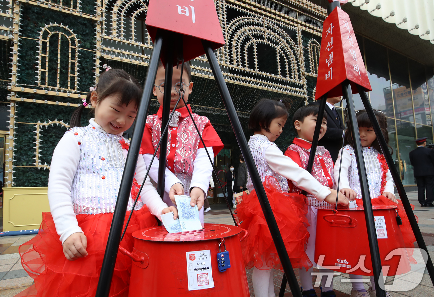 (부산=뉴스1) 윤일지 기자 = 1일 부산 부산진구 롯데백화점 부산본점 정문 앞 광장에서 열린 구세군 자선냄비 시종식에서 축하공연을 펼친 어린이들이 자선냄비에 돈을 넣고 있다.구세 …