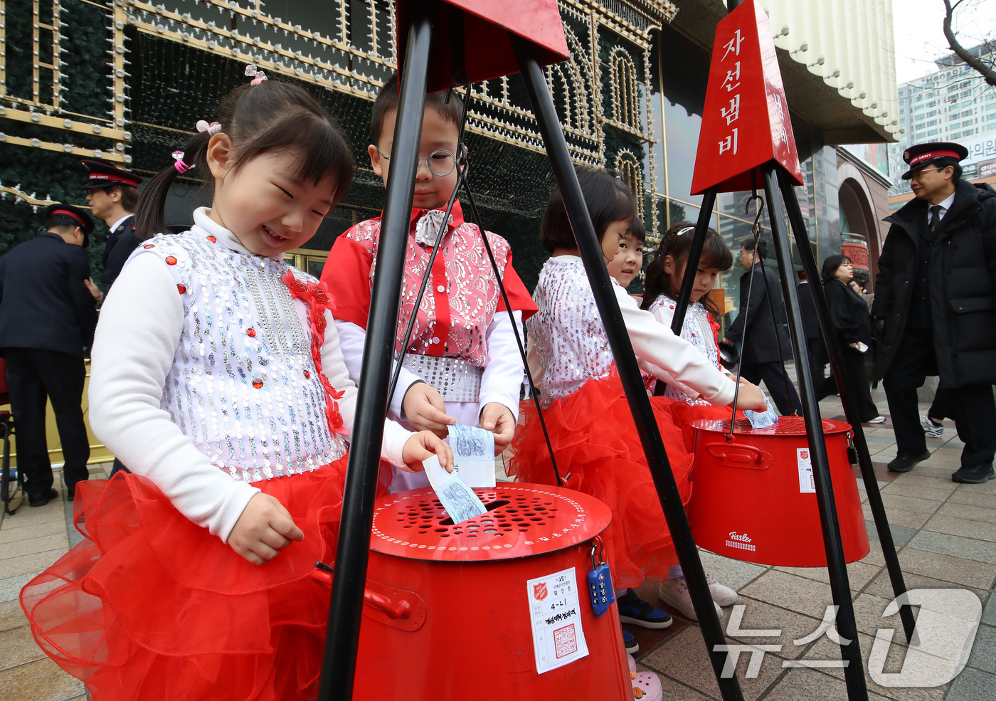 (부산=뉴스1) 윤일지 기자 = 1일 부산 부산진구 롯데백화점 부산본점 정문 앞 광장에서 열린 구세군 자선냄비 시종식에서 축하공연을 펼친 어린이들이 자선냄비에 돈을 넣고 있다.구세 …