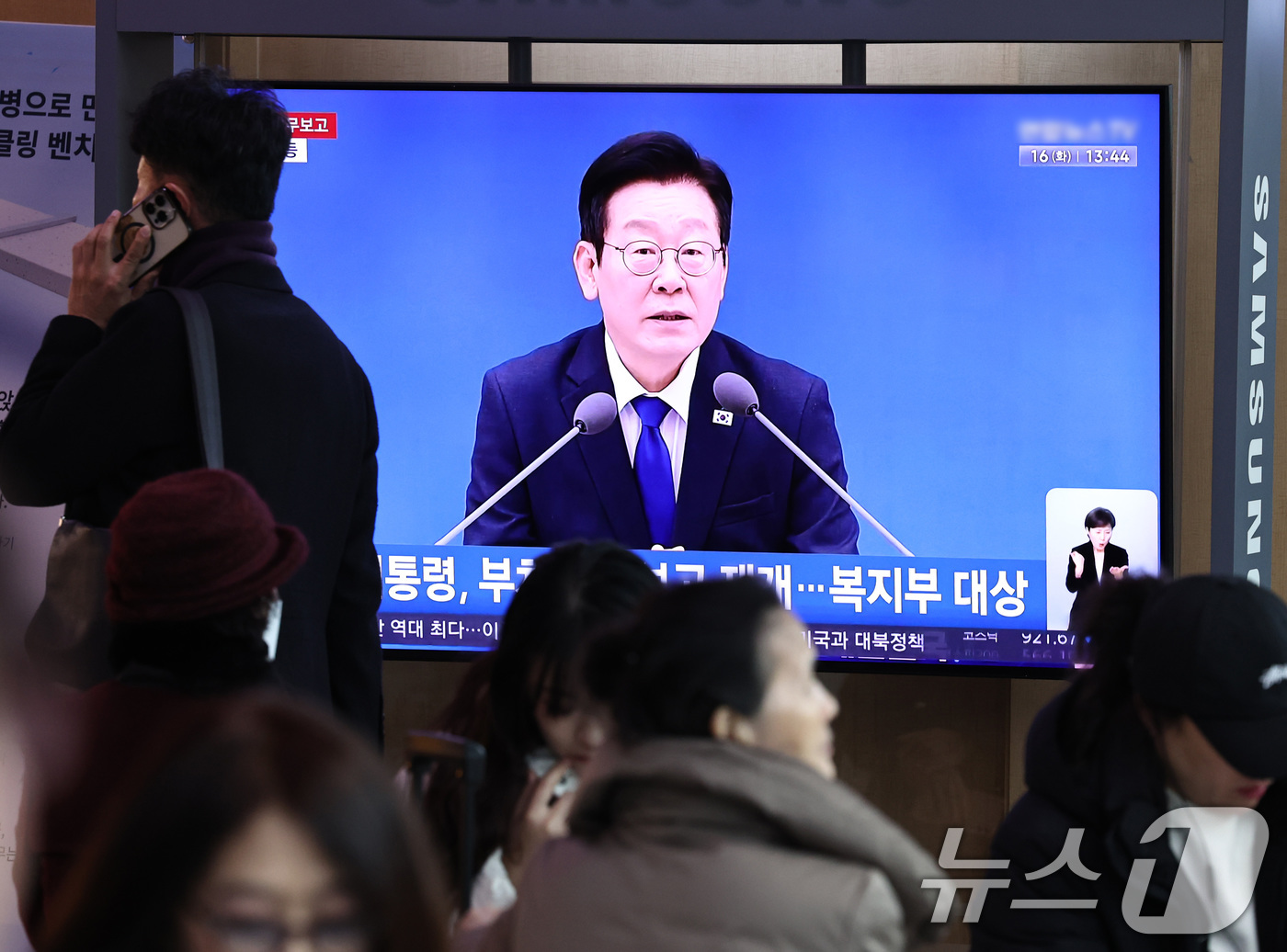 (서울=뉴스1) 구윤성 기자 = 16일 오후 서울 용산구 서울역 대합실 텔레비전을 통해 이재명 대통령의 보건복지부 등에 대한 업무보고 영상이 생중계되고 있다.  2025.12.16 …