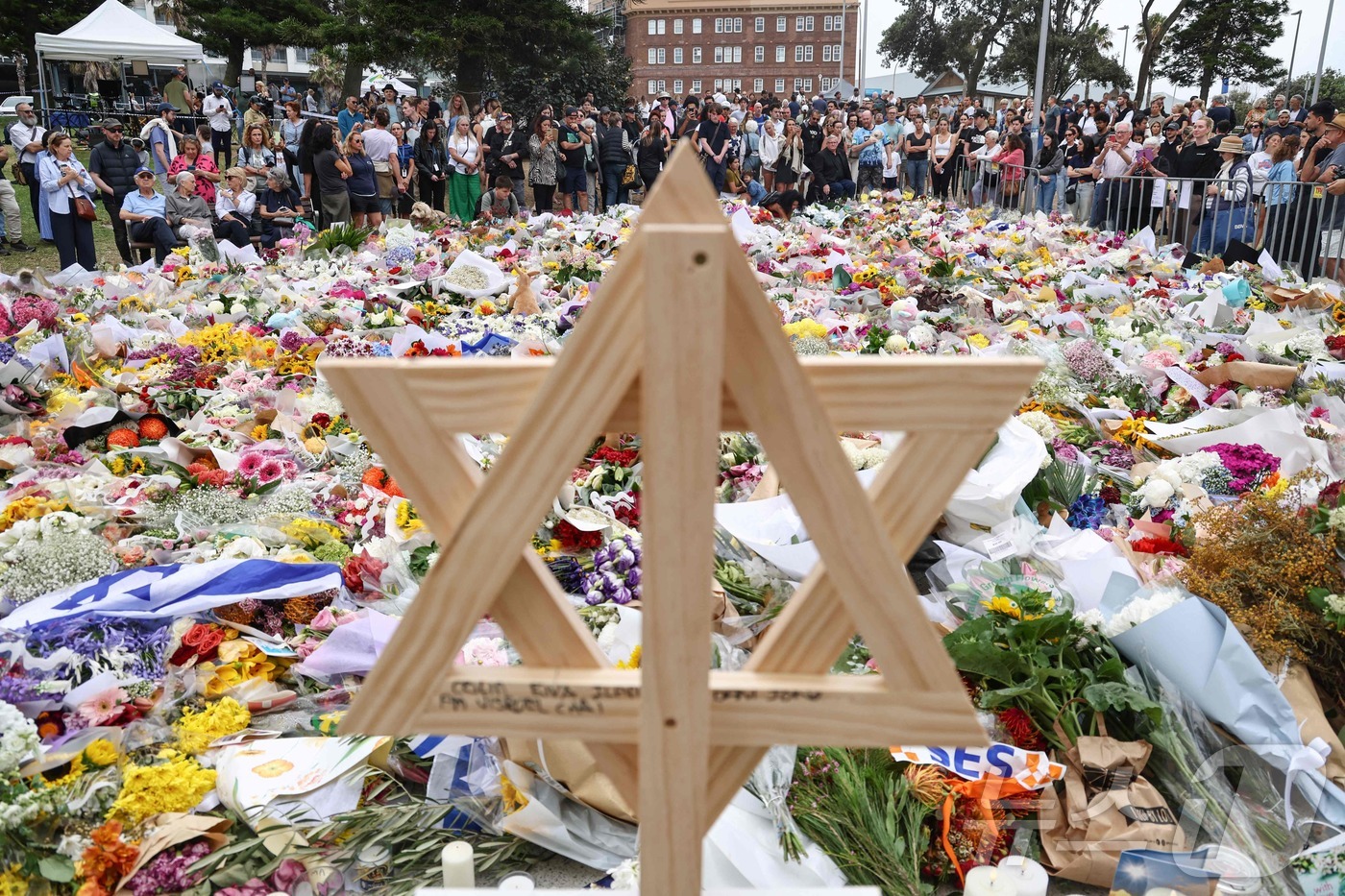 (시드니 AFP=뉴스1) 권영미 기자 = 16일 호주 시드니의 본다이 파빌리온 앞에 본다이 비치 총격 사건 희생자를 추모하기 위해 모인 사람들 사이로 나무로 만든 다윗의 별이 보인 …