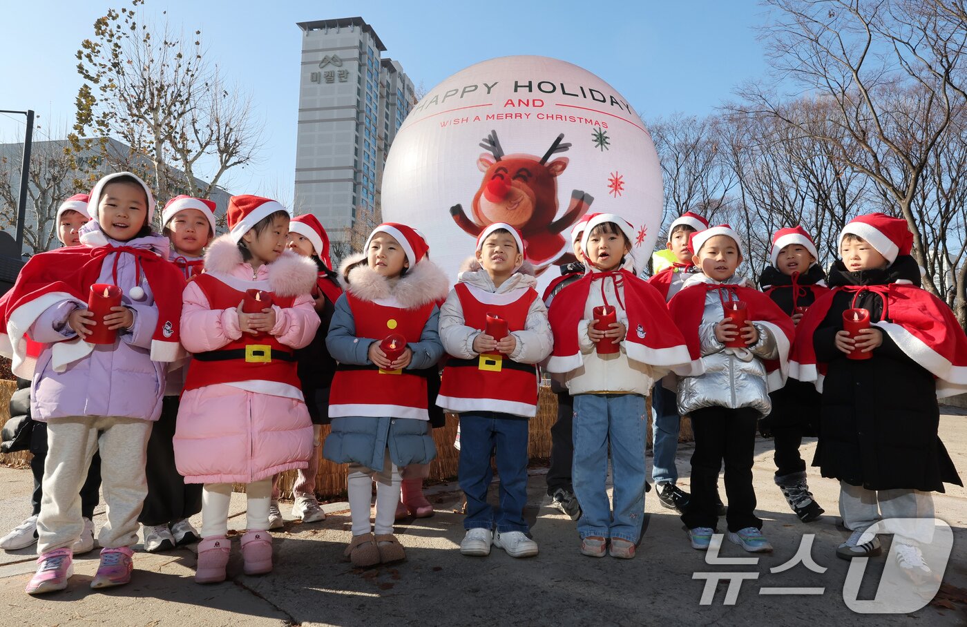 본문 이미지 - 산타 복장을 차려입은 송파구청 어린이집 아이들이 18일 오전 서울 송파구 석촌호수 더 스피어에서 크리스마스 캐럴을 부르고 있다. 2025.12.18/뉴스1 ⓒ News1 장수영 기자