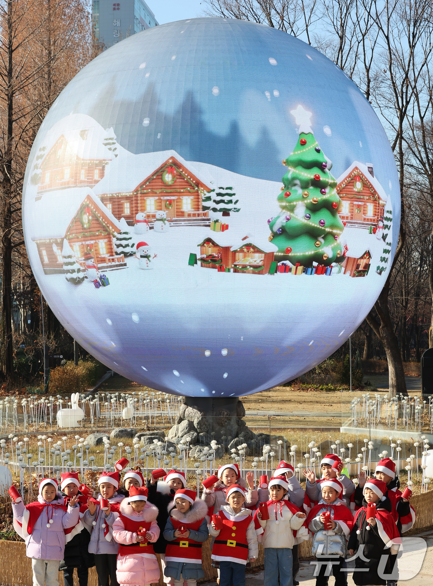 (서울=뉴스1) 장수영 기자 = 산타 복장을 차려입은 송파구청 어린이집 아이들이 18일 오전 서울 송파구 석촌호수 더 스피어에서 손을 흔들고 있다.송파구는 연말연시를 맞아 더 스피 …