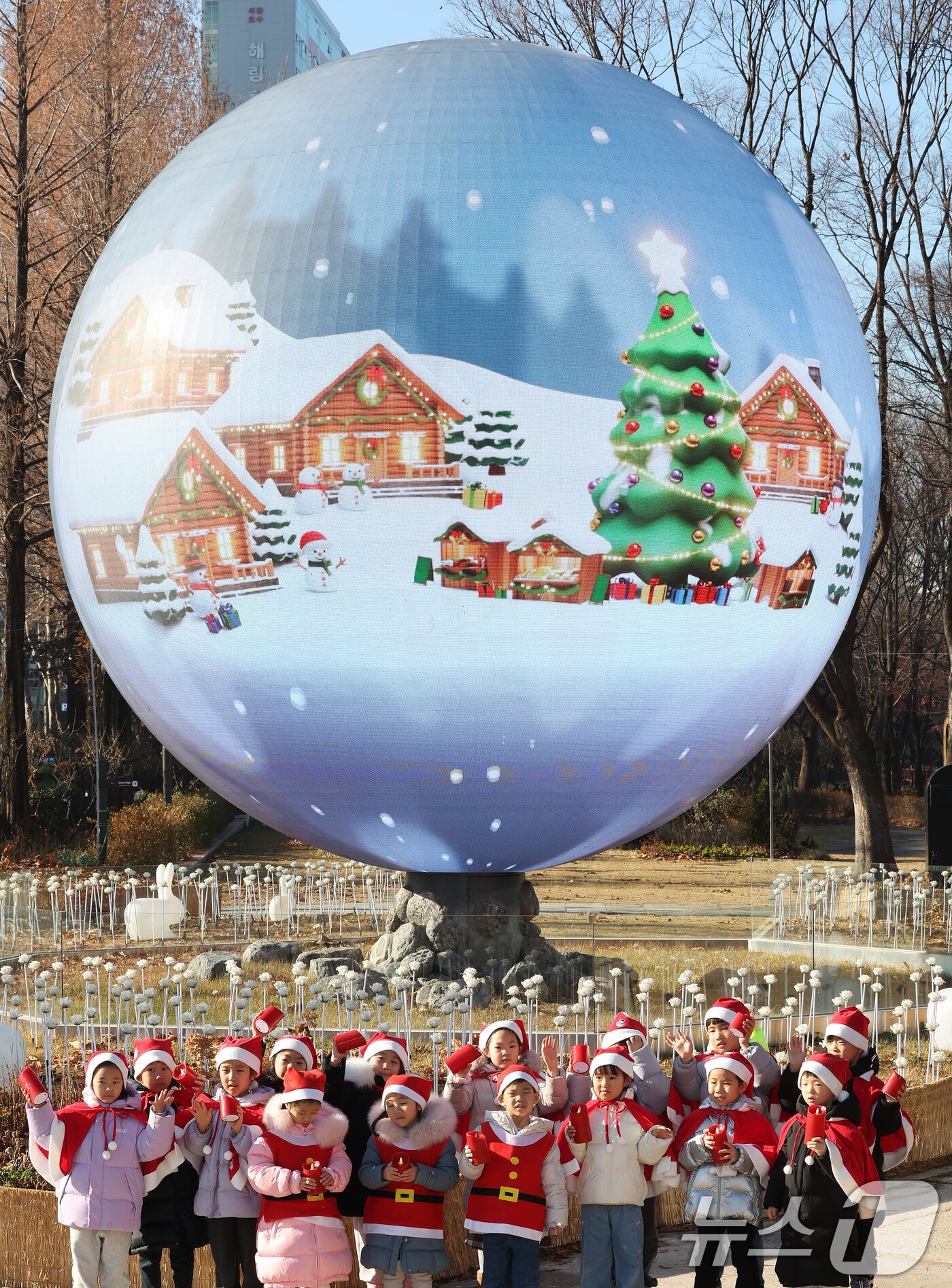 본문 이미지 - 산타 복장을 차려입은 송파구청 어린이집 아이들이 18일 오전 서울 송파구 석촌호수 더 스피어에서 손을 흔들고 있다. 2025.12.18/뉴스1 ⓒ News1 장수영 기자