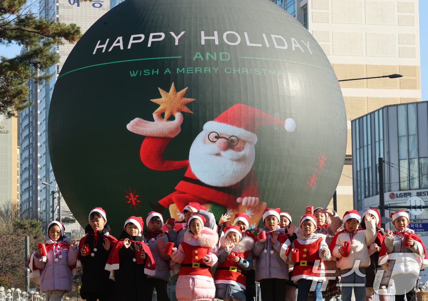 본문 이미지 - 산타 복장을 차려입은 송파구청 어린이집 아이들이 18일 오전 서울 송파구 석촌호수 더 스피어에서 손을 흔들고 있다.  2025.12.18/뉴스1 ⓒ News1 장수영 기자