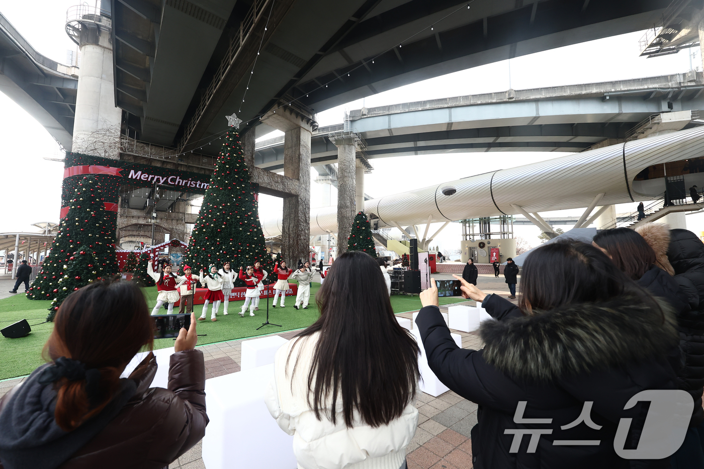 (서울=뉴스1) 김민지 기자 = 19일 오후 서울 뚝섬한강공원 자벌레 서울생각마루 인근에서 열린 2025 로맨틱 한강 크리스마스 마켓에서 시민들이 어린이 합창단 공연을 보고 있다. …