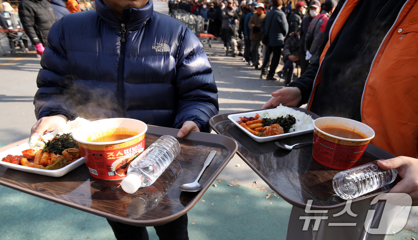 (대구=뉴스1) 공정식 기자 = 초겨울 추위가 찾아온 2일 오전 대구 달서구 두류공원 사랑해밥차 무료급식소에서 점심 배식 식판을 받은 사람들이 식사할 곳으로 이동하고 있다. 202 …