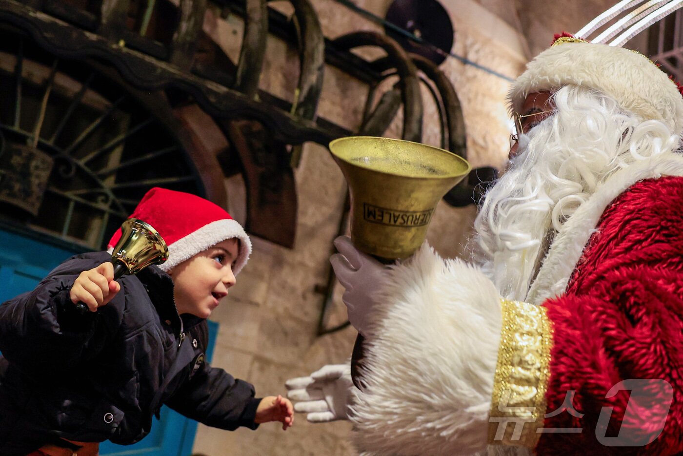 본문 이미지 - 지난 14일(현지시간) 팔레스타인 서안지구 베들레헴에서 열린 크리스마스 퍼레이드에서 산타클로스 복장을 한 사람이 아이에게 인사를 건네고 있다. 2025.12.14. ⓒ 로이터=뉴스1 ⓒ News1 이정환 기자