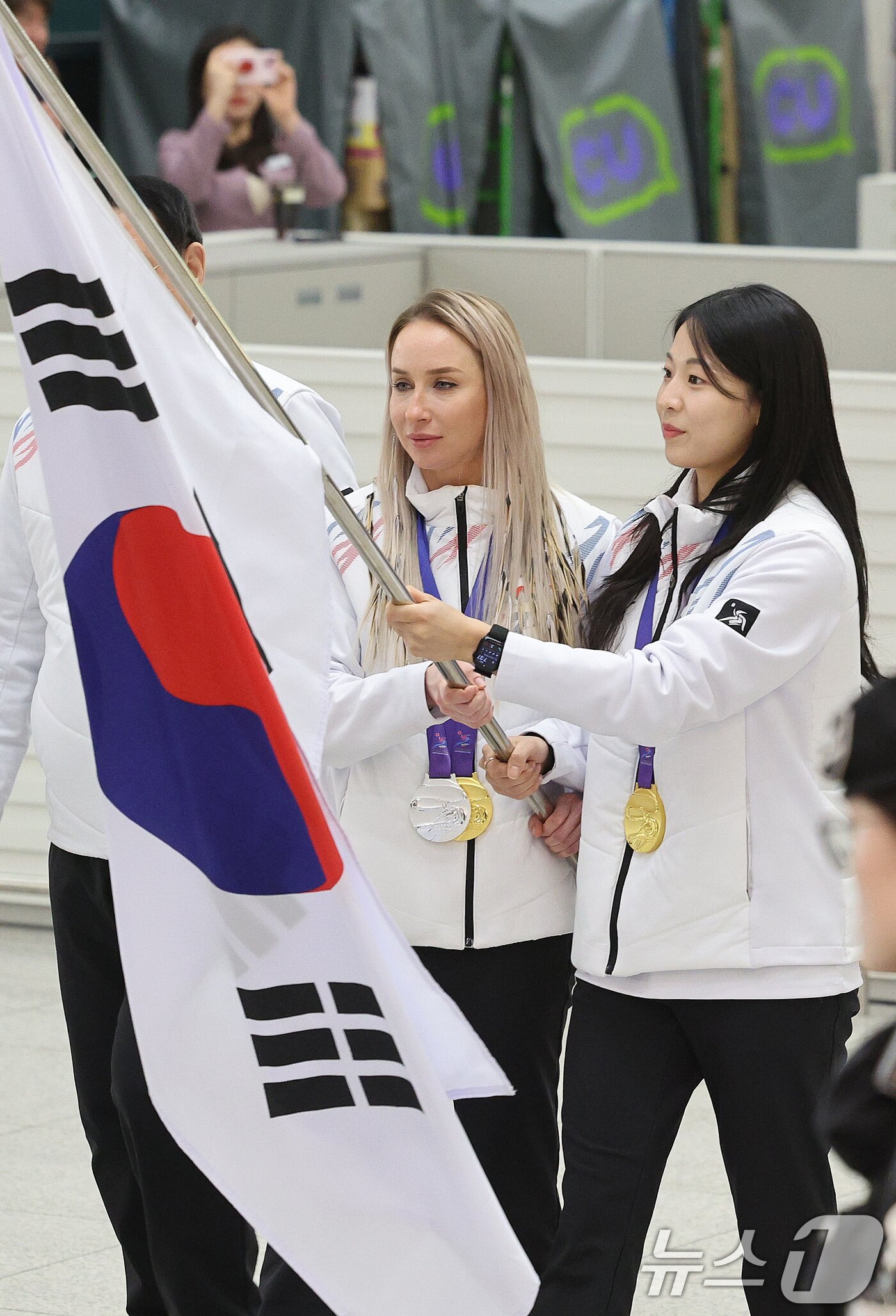 본문 이미지 - 귀화 선수로서 한국 바이애슬론 사상 첫 동계아시안게임 금메달을 획득한 예카테리나 압바꾸모바&#40;왼쪽&#41;와 여자컬링에서 금메달을 차지한 김민지가 15일 오후 인천국제공항 1터미널 귀국장에서 열린 2025 하얼빈 동계 아시안게임 한국 선수단 귀국 환영 행사에 태극기를 들고 입장하고 있다. 8년 만에 열린 이번 대회에 한국은 총 222명의 선수단을 파견해 금메달 16개, 은메달 15개, 동메달 14개를 수확하며 개최국 중국&#40;금 32·은 27·동 25&#41;에 이어 종합 2위를 차지했다. 2025.2.15/뉴스1 ⓒ News1 신웅수 기자