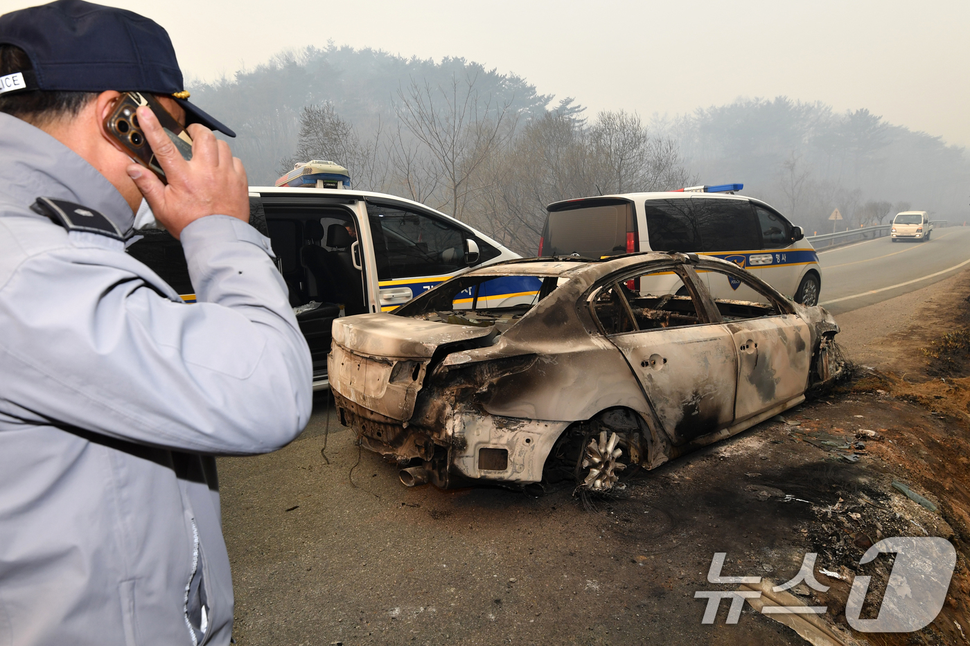 (영덕=뉴스1) 최창호 기자 = 26일 경북 영덕군 매정리 마을로 들어가는 도로에서 경찰관이 불에 탄 승용차를 확인하고 있다.경찰은 산불이 확산되자 승용차로 대피하던 요양원 입소자 …