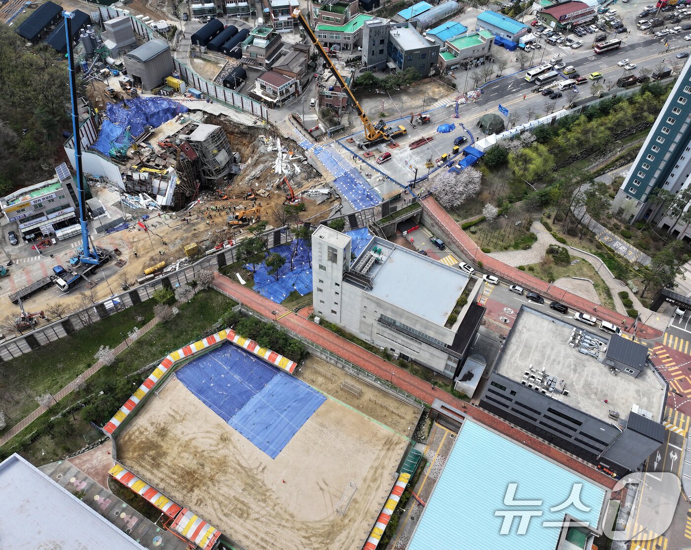 본문 이미지 - 16일 경기 광명시 일직동 신안산선 복선전철 5-2공구 붕괴 현장과 인근 초등학교 운동장에 깔린 균열 부위 방수포가 함께 보이고 있다. 2025.4.16/뉴스1 ⓒ News1 이동해 기자