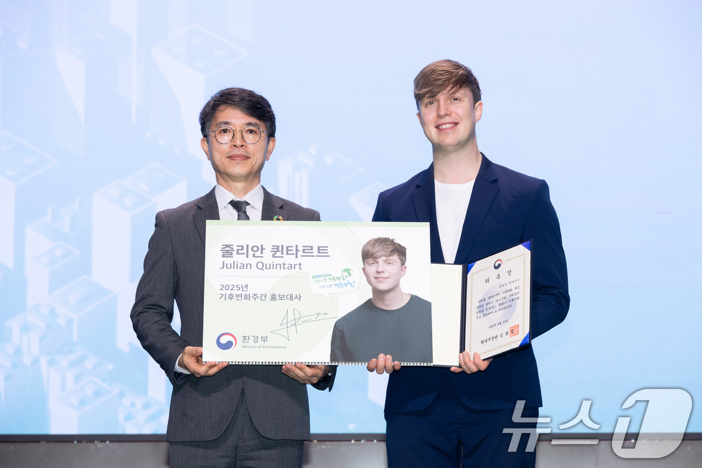 (서울=뉴스1) = 김완섭 환경부 장관이 21일 서울 강서구 코엑스 마곡에서 열린 2025년 기후변화주간 개막식에 참석해 벨기에 출신 방송인 줄리안 퀸타르트에게 기후변화주간 홍보대 …