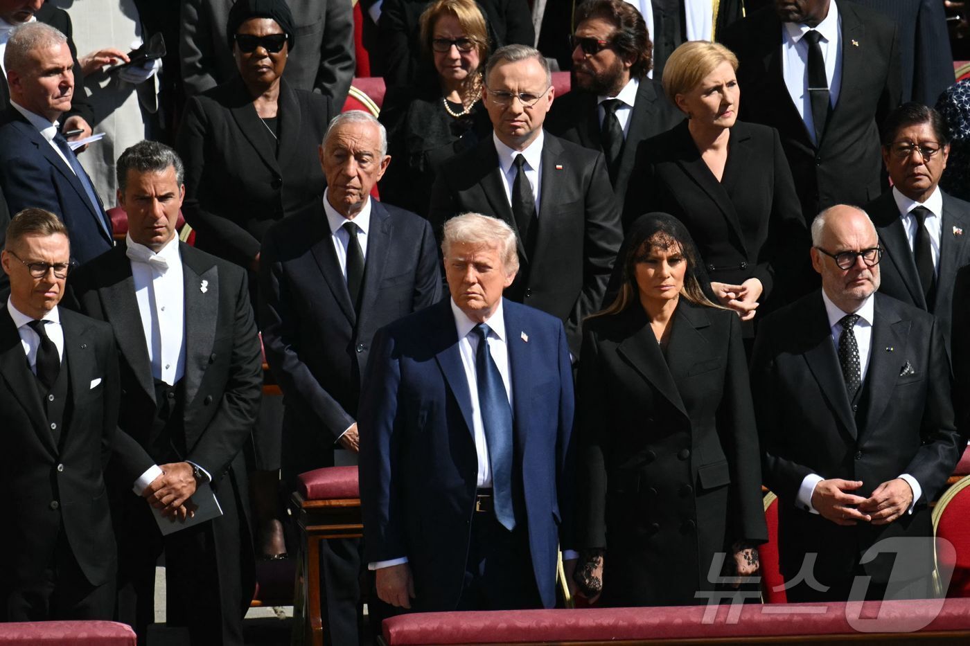 본문 이미지 - 도널드 트럼프 미국 대통령과 부인 멜라니아 여사가 26일 &#40;현지시간&#41; 바티칸의 성 베드로 광장에서 열린 프란치스코 교황의 장례 미사에 참석해 기립을 하고 있다. 2025.04,27 ⓒ AFP=뉴스1 ⓒ